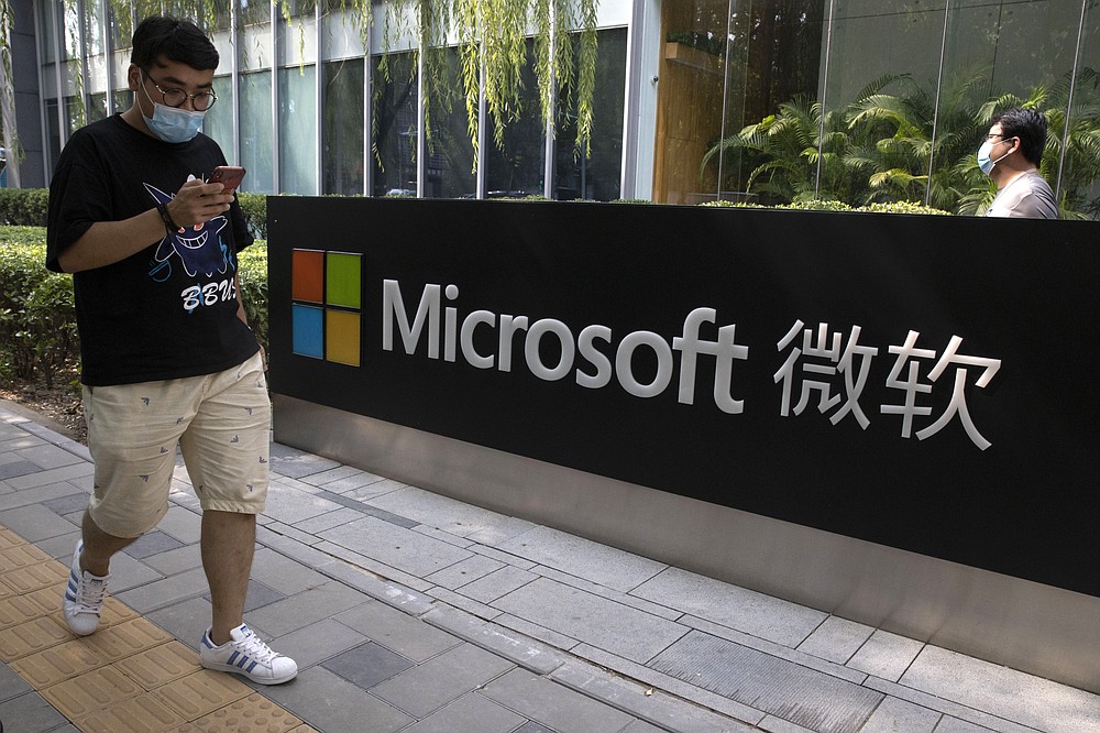 A man looks at his smartphone as he walks by the Microsoft office in Beijing, China on Friday, Aug. 7, 2020. The Biden administration on Monday, July 19, 2021 blamed China for a hack of Microsoft Exchange email server software that compromised tens of thousands of computers around the world earlier this year. (AP Photo/Ng Han Guan)